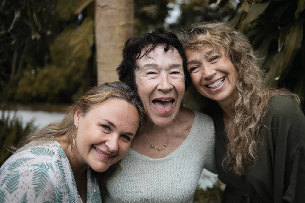 Trois générations de femmes réunies, souriantes et complices, posant dans un cadre végétal.