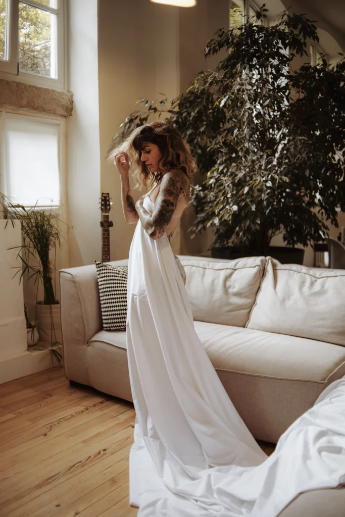 Femme en robe blanche fluide posant dans un intérieur lumineux et végétalisé.
