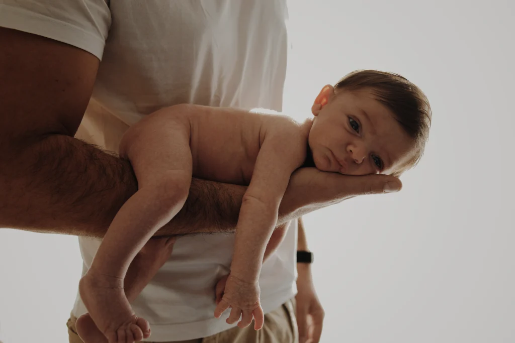 Nouveau-né reposant sur le bras de son père, moment de tendresse capturé en lumière naturelle.