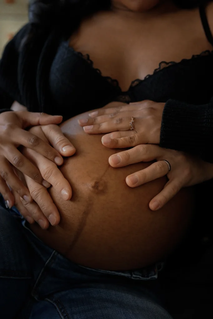 Deux futurs parents, posant tendrement leurs mains entrelacées sur le ventre rond de la mère, lors d'une séance photo grossesse.