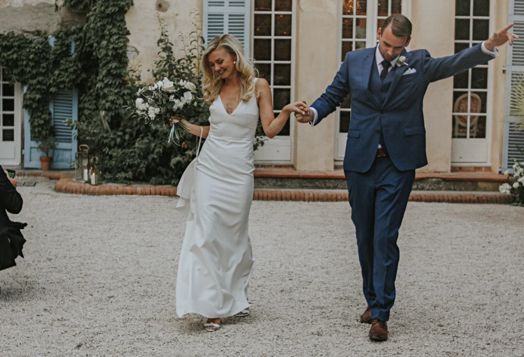 Mariée radieuse en robe blanche épurée tenant son bouquet de fleurs blanches