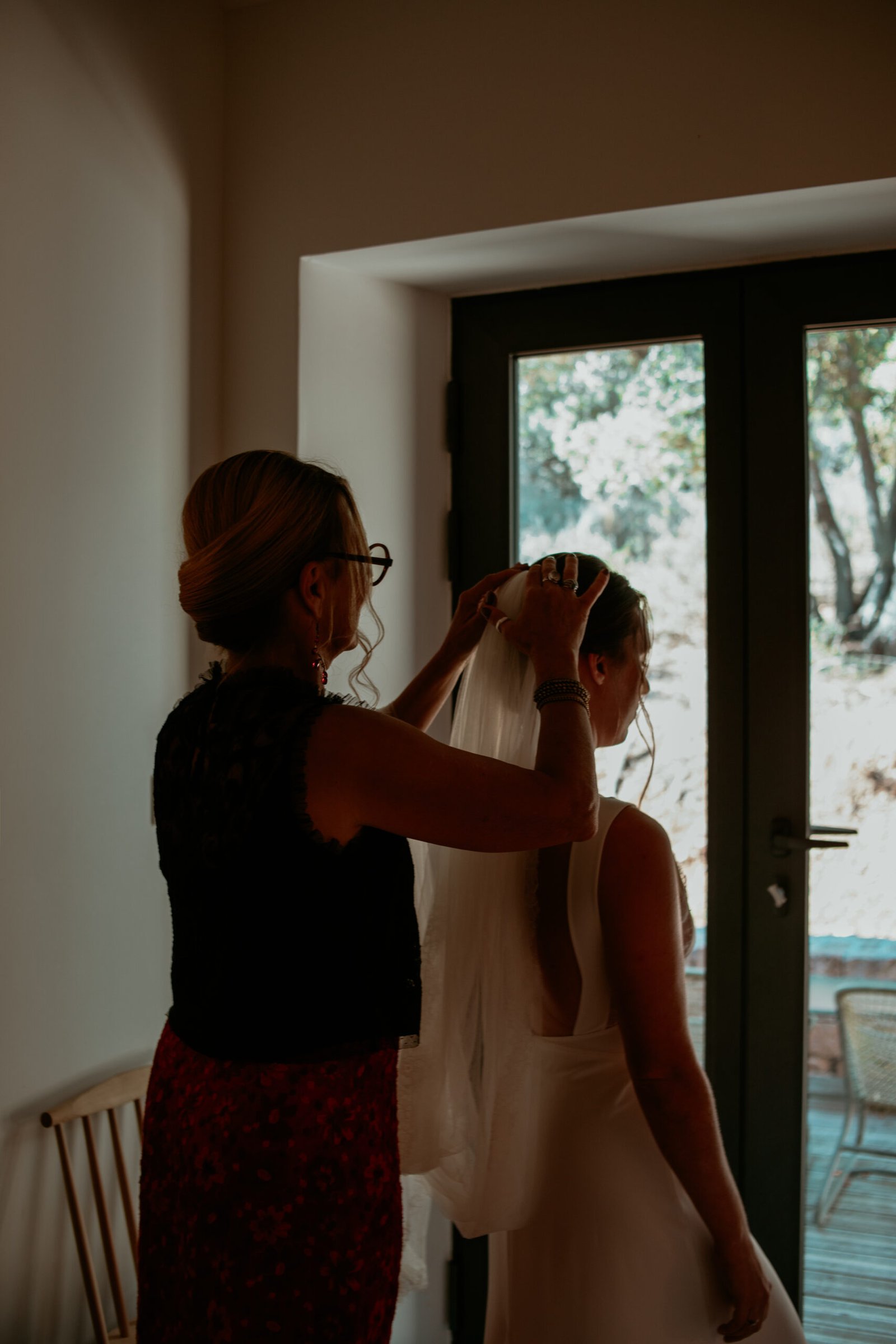 Préparation de la mariée, ajustement du voile devant une fenêtre. Photographe mariage naturel et discret Provence.