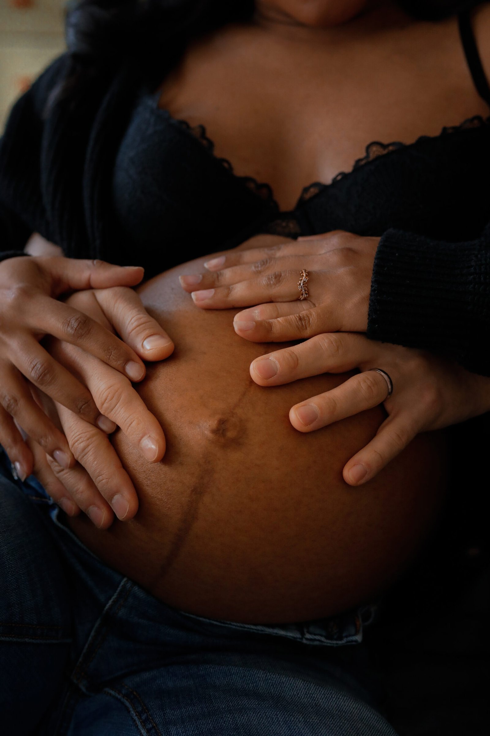 Ventre rond d'une femme enceinte, sur lequel sont posées les mains jointes des futurs parents.