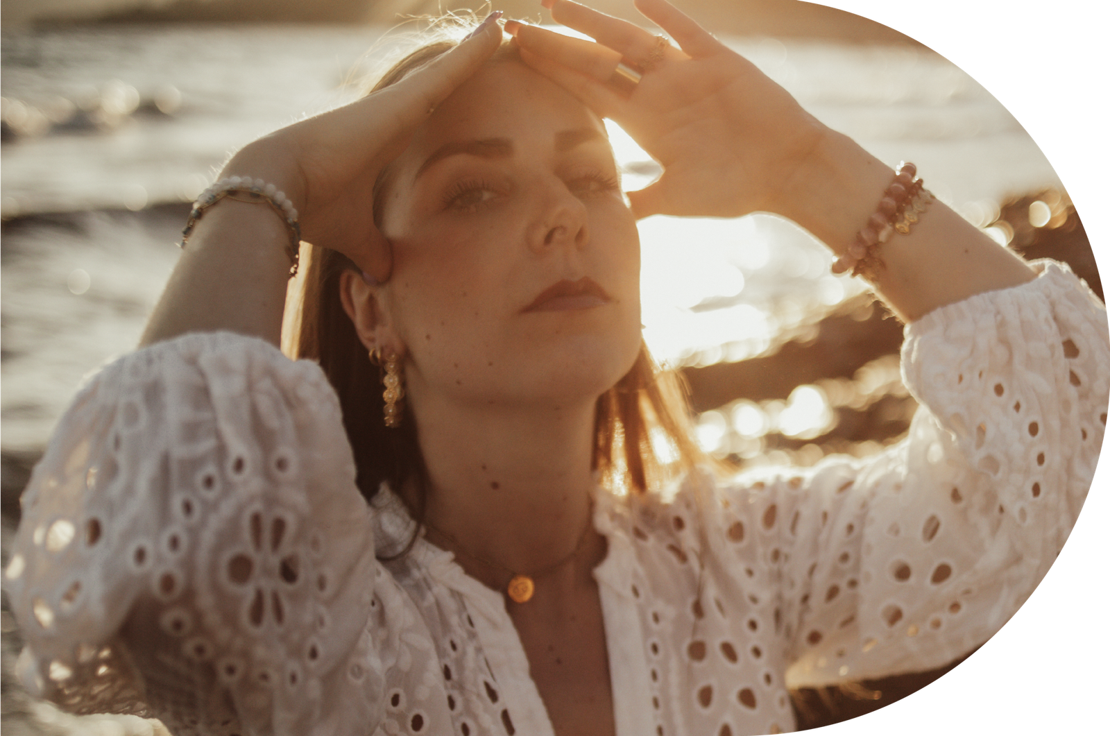 Shooting photo solo femme Provence. Une femme agenouillée au bord de l'eau, portant ses mains à ses cheveux sous le coucher du soleil.