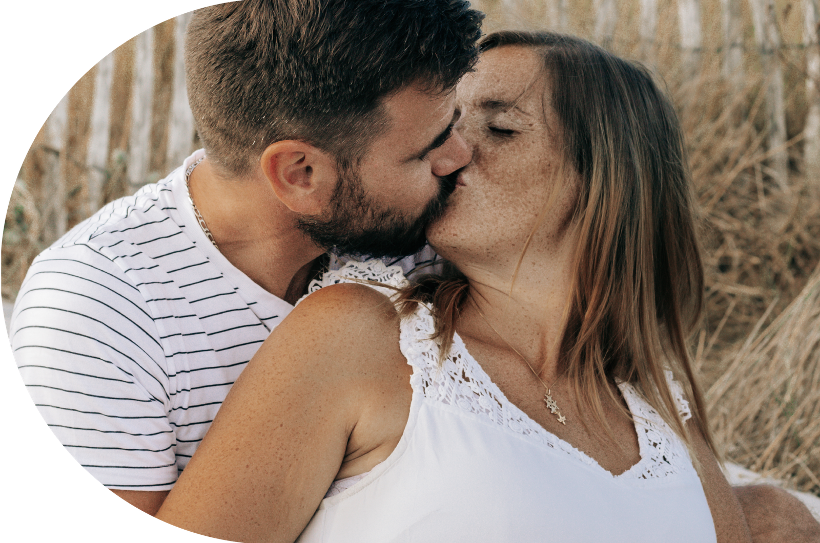 Un jeune couple, s'embrassant tendrement sur la plage, leurs mains entrelacées et posées sur le ventre de la femme.