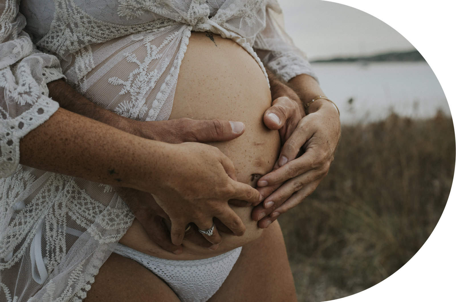 De futurs parents lors d'une séance grossesse sur la plage, sans un ciel gris.