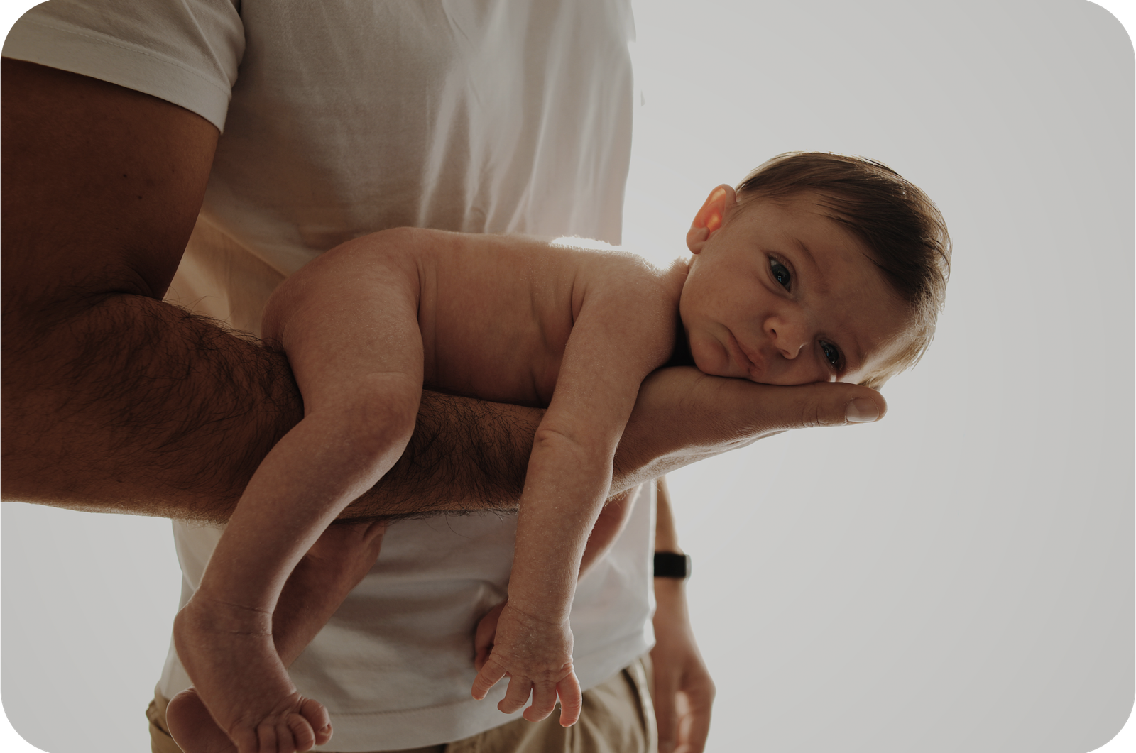 Un bébé, posé sur le bras de son père, l'air apaisé.