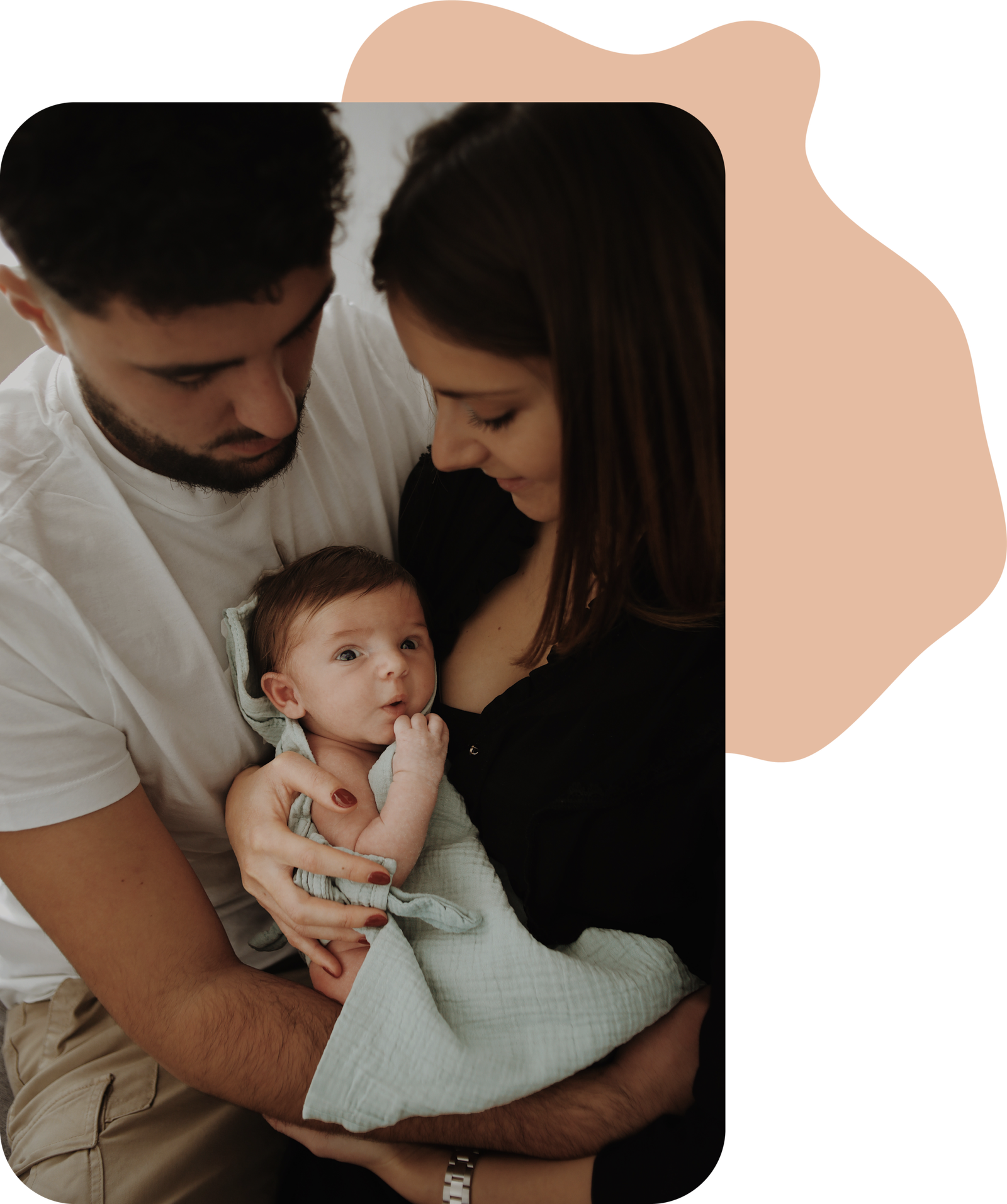 Deux parents, tenant dans leurs bras leur fils, l'air surpris devant la caméra. Une séance famille à domicile.