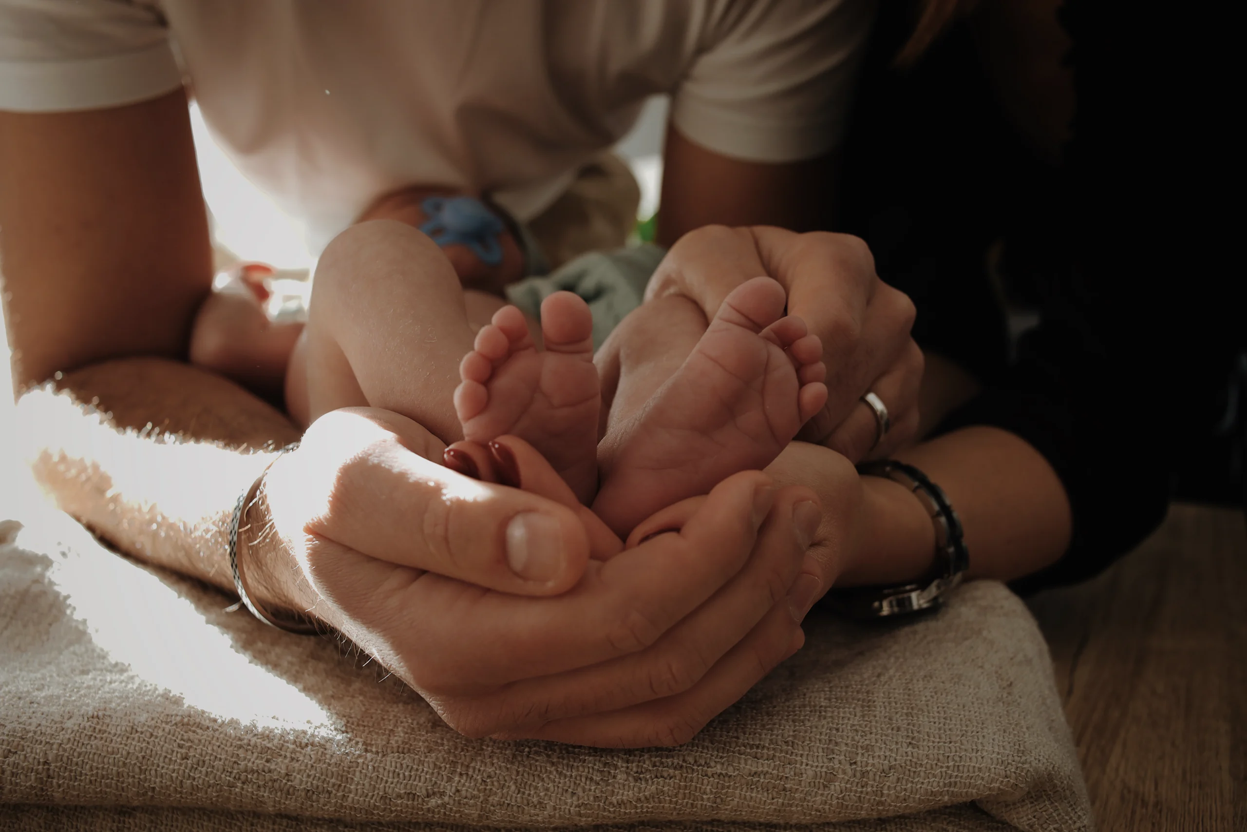 Les pieds d'un nouveau né, posés dans les mains jointes de ses parents. Un moment tendre et doux durant une séance photo naissance lifestyle.