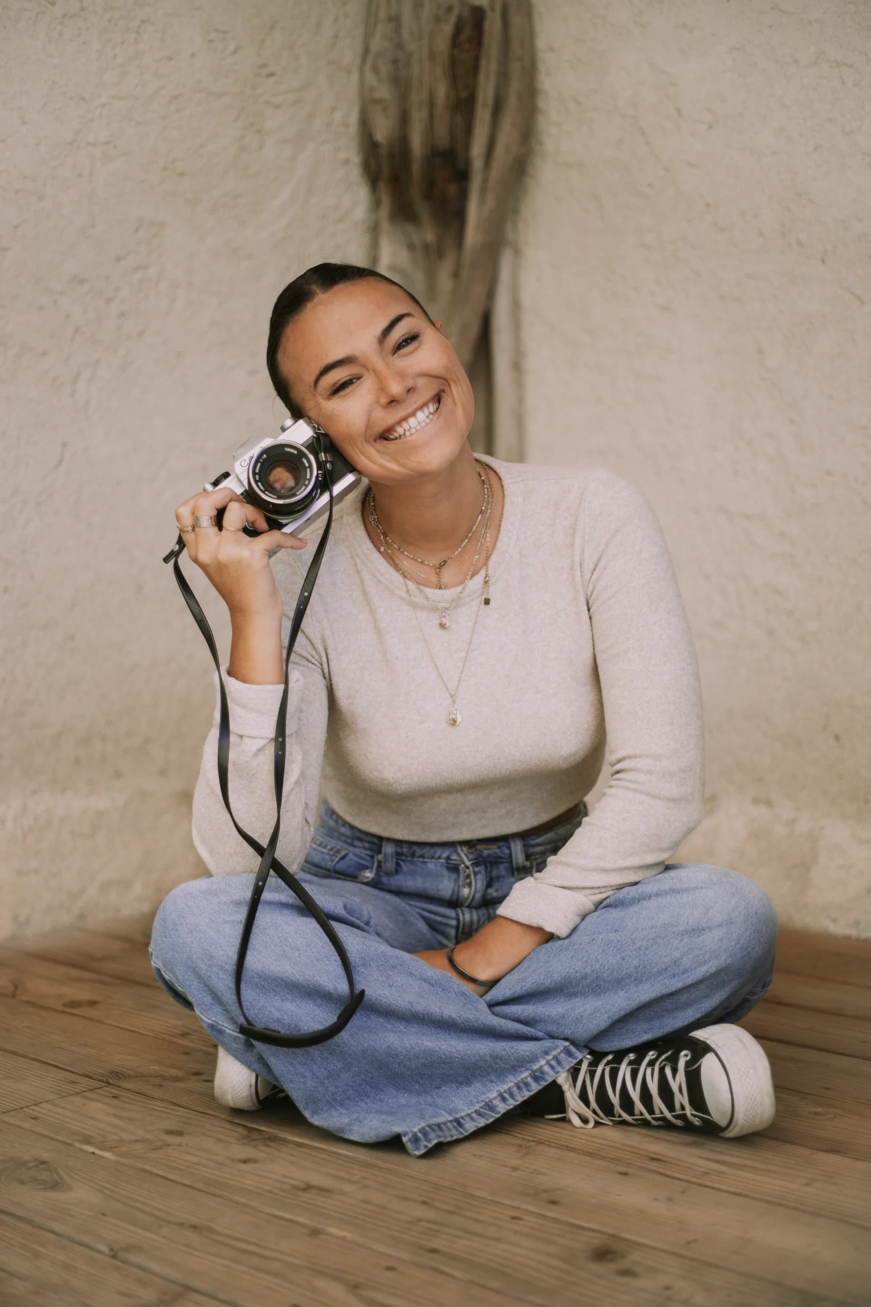 Nolwenn Biannic Photographe, assise en tailleur, appuyant sa tête sur son appareil photo et riant. Elle aime construire de vraie relation client photographe.