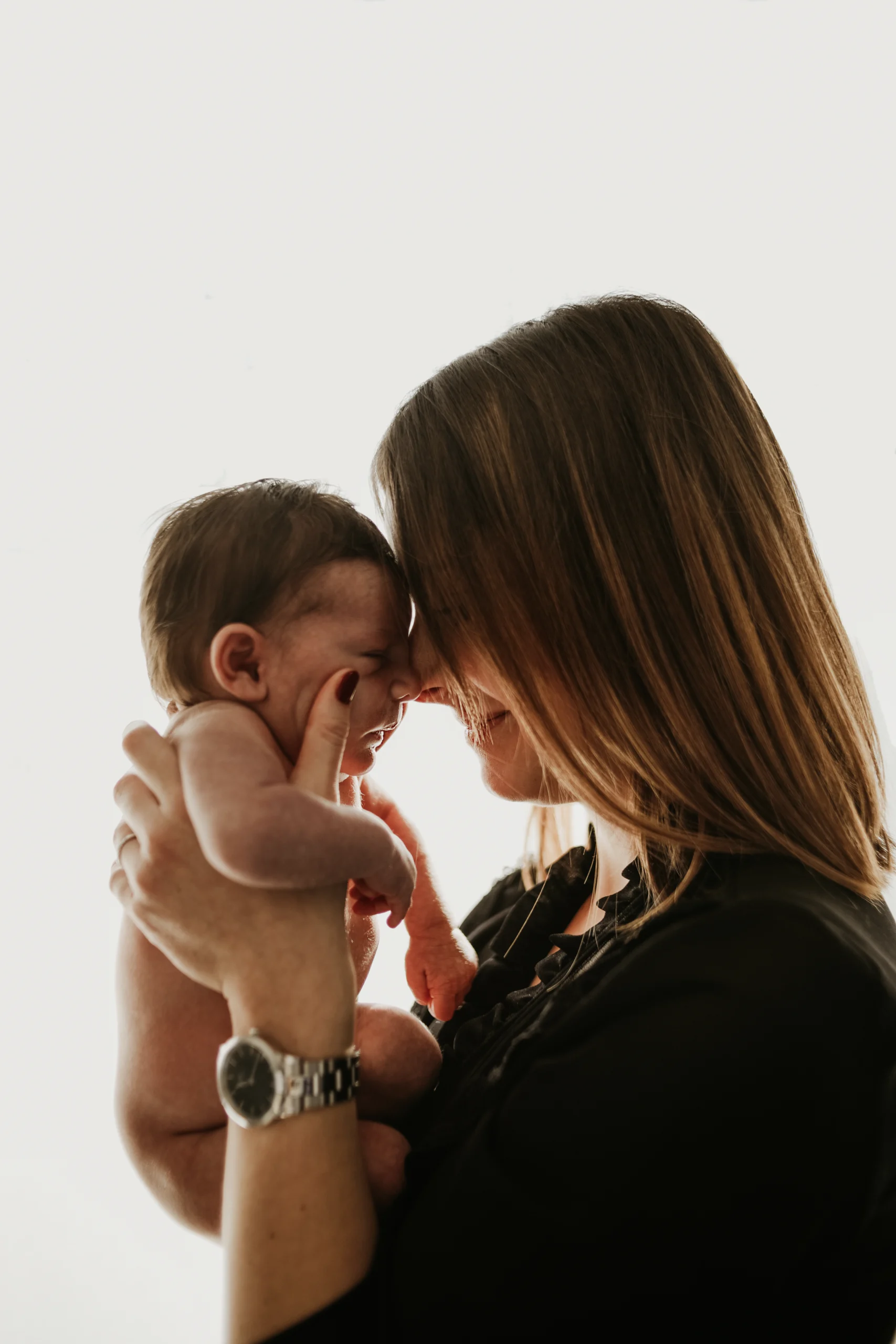Une mère tenant son nouveau né près de sa tête et le regaardant avec le sourire lors d'une séance photo naissance lifestyle à domicile.