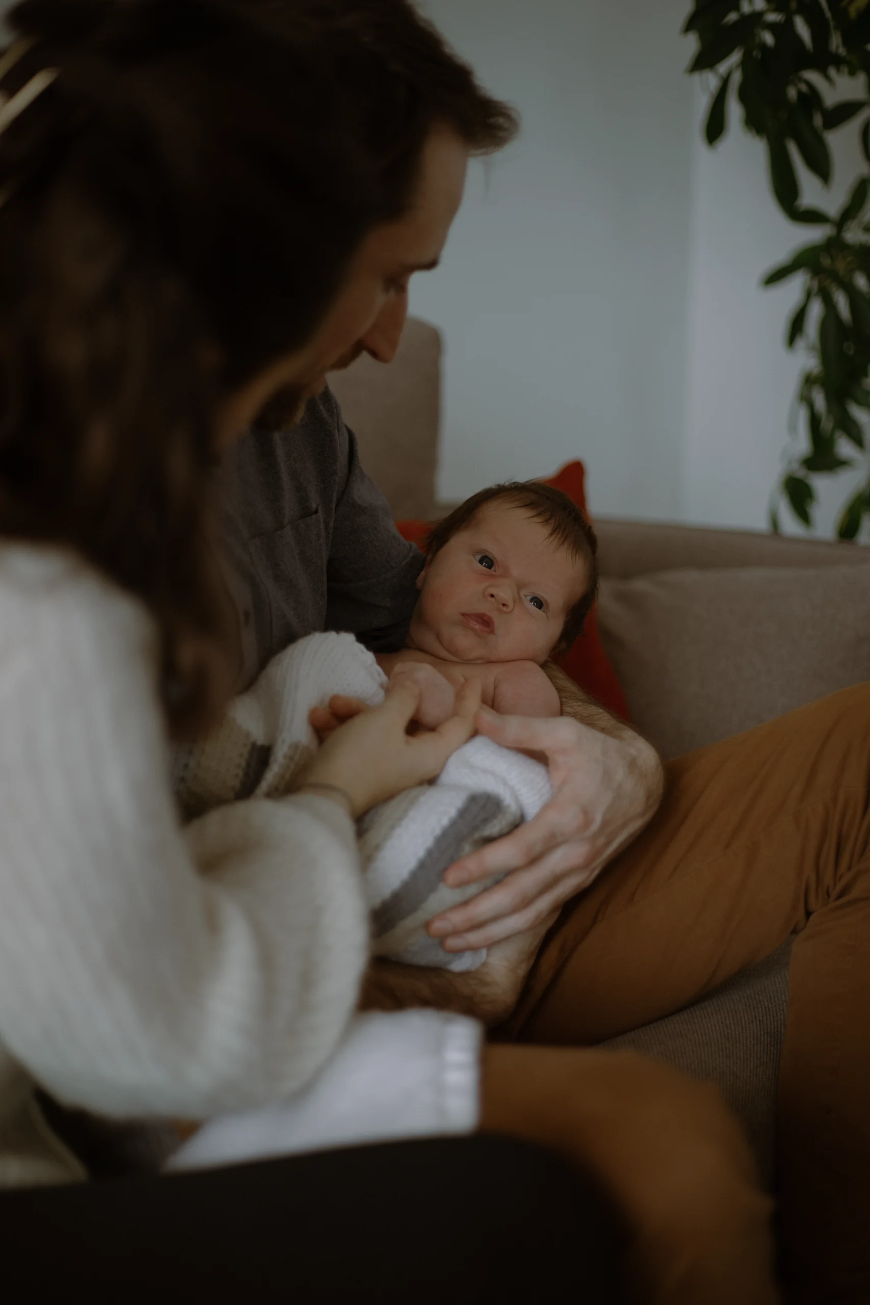 Un nouveau né, dans les bras de ses parents, qui le regardent avec amour. Une séance photo naissance lifestyle.