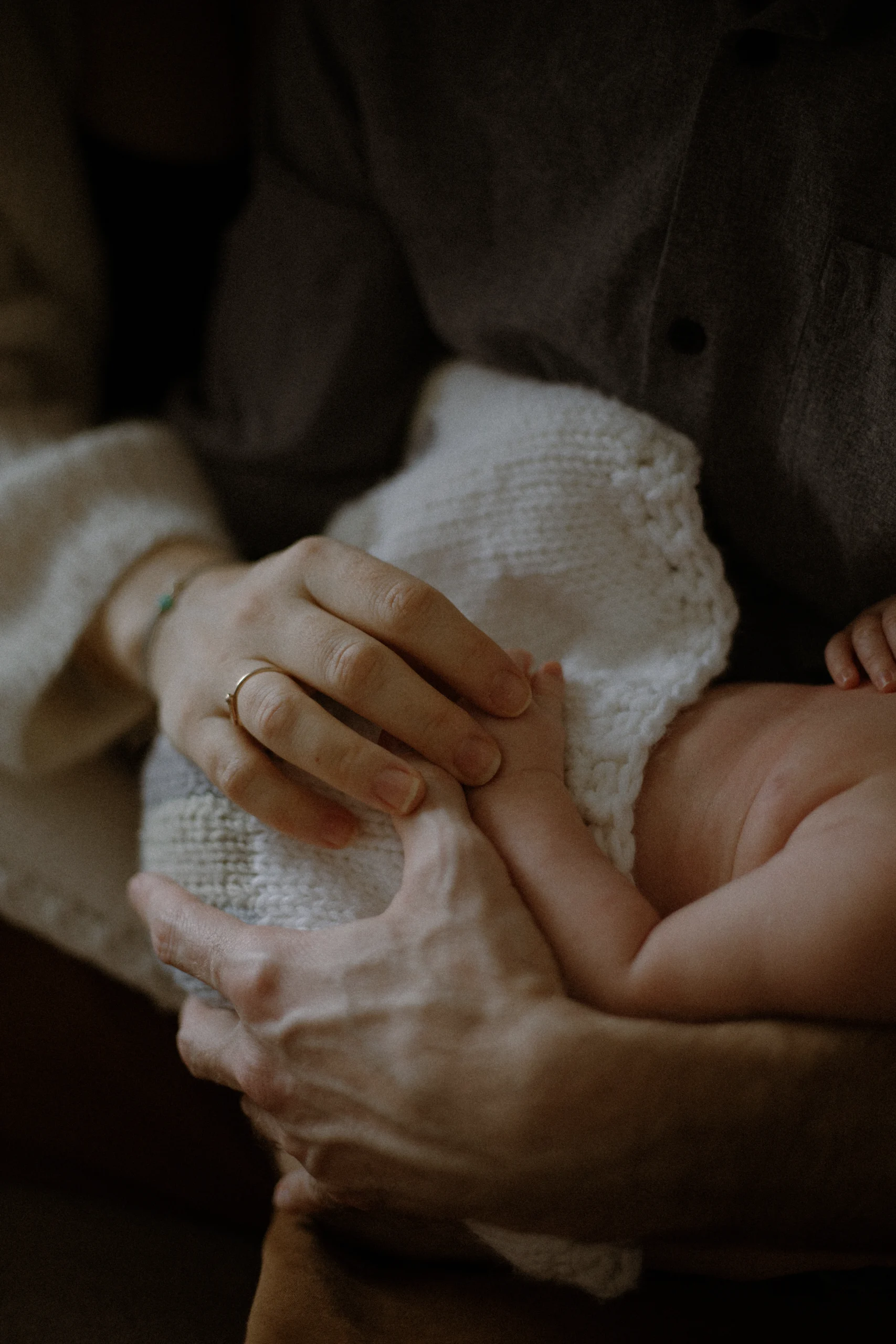 Les deux de deux parents, tenant celle de leur nouveau né, enveloppé d'une couverture en tricot blanc. Une séance photo naissance lifestyle.