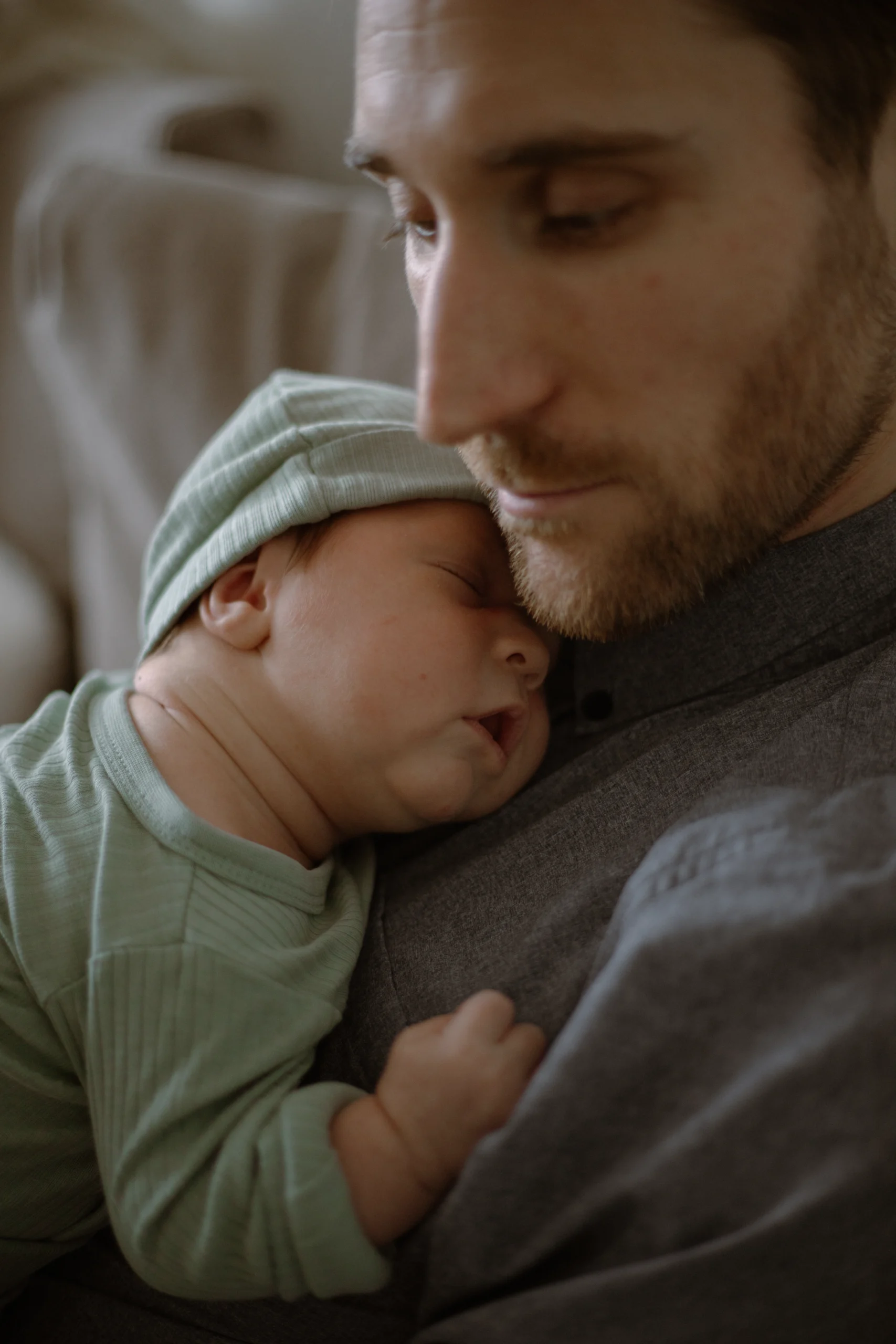 Un père, tenant dans ses bras son bébé endormi. Un moment tendre lors d'une séance photo naissance lifestyle.