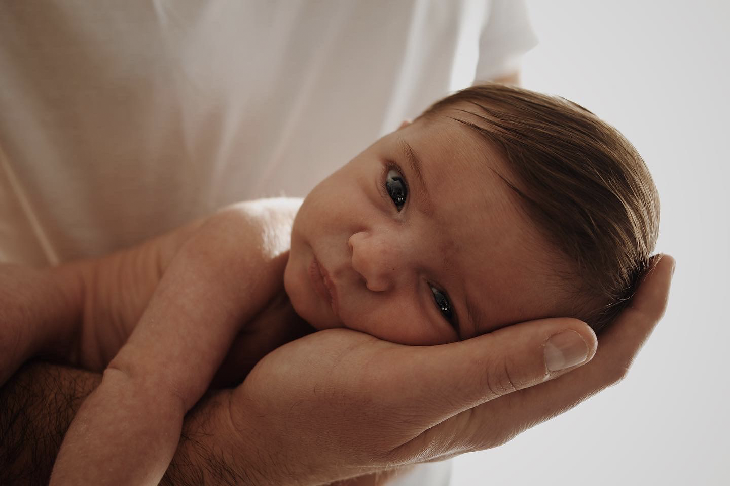 Un bébé posé sur le ventre sur le bras de son père, la tête dans la paume de sa main. Une séance photo naissance lifestyle douce.