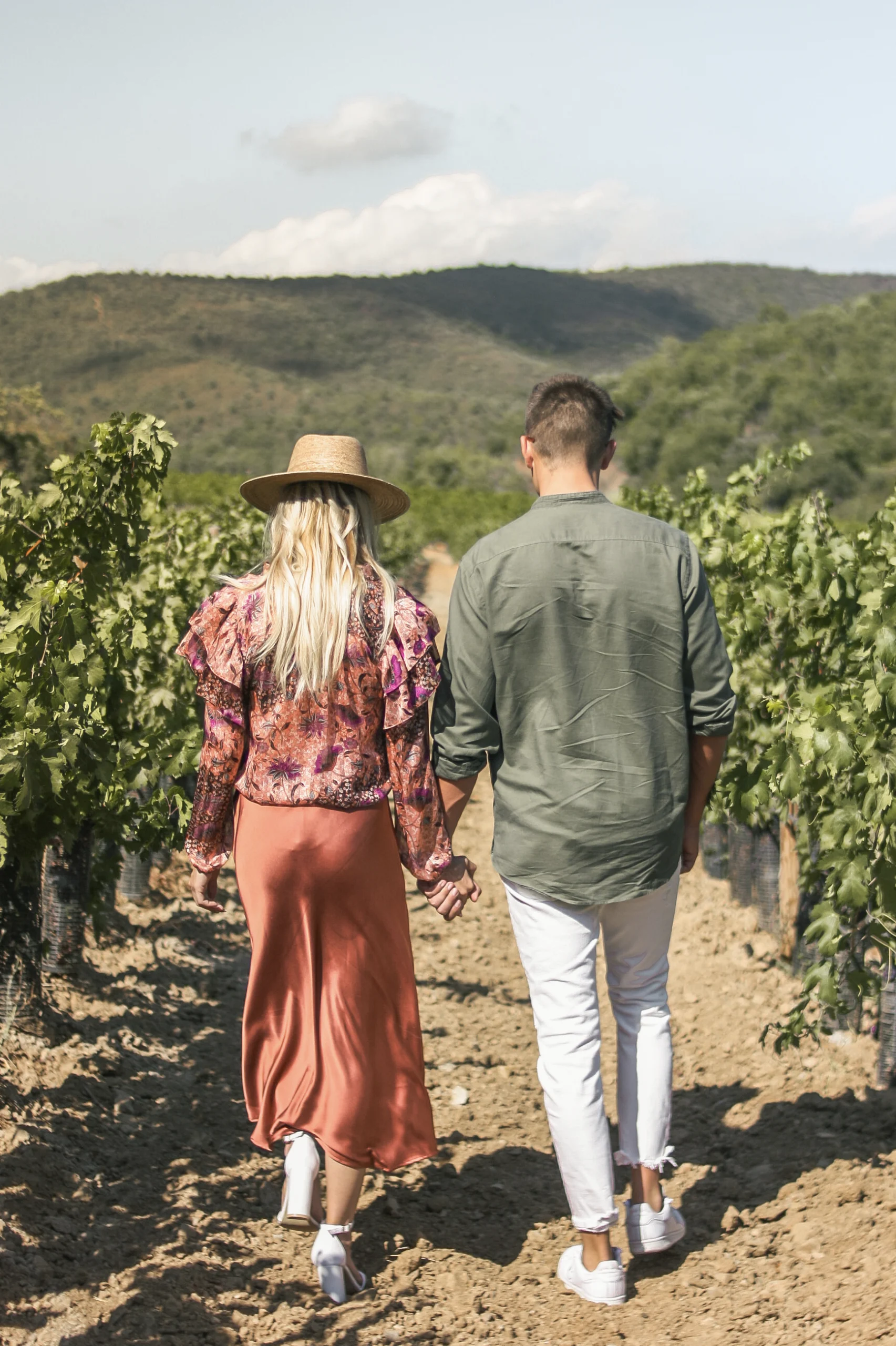 Un couple marchant de dos dans des rangées de vignes. Ils se tiennent la main et partage un moment unique pendant leur séance engagement en Provence.