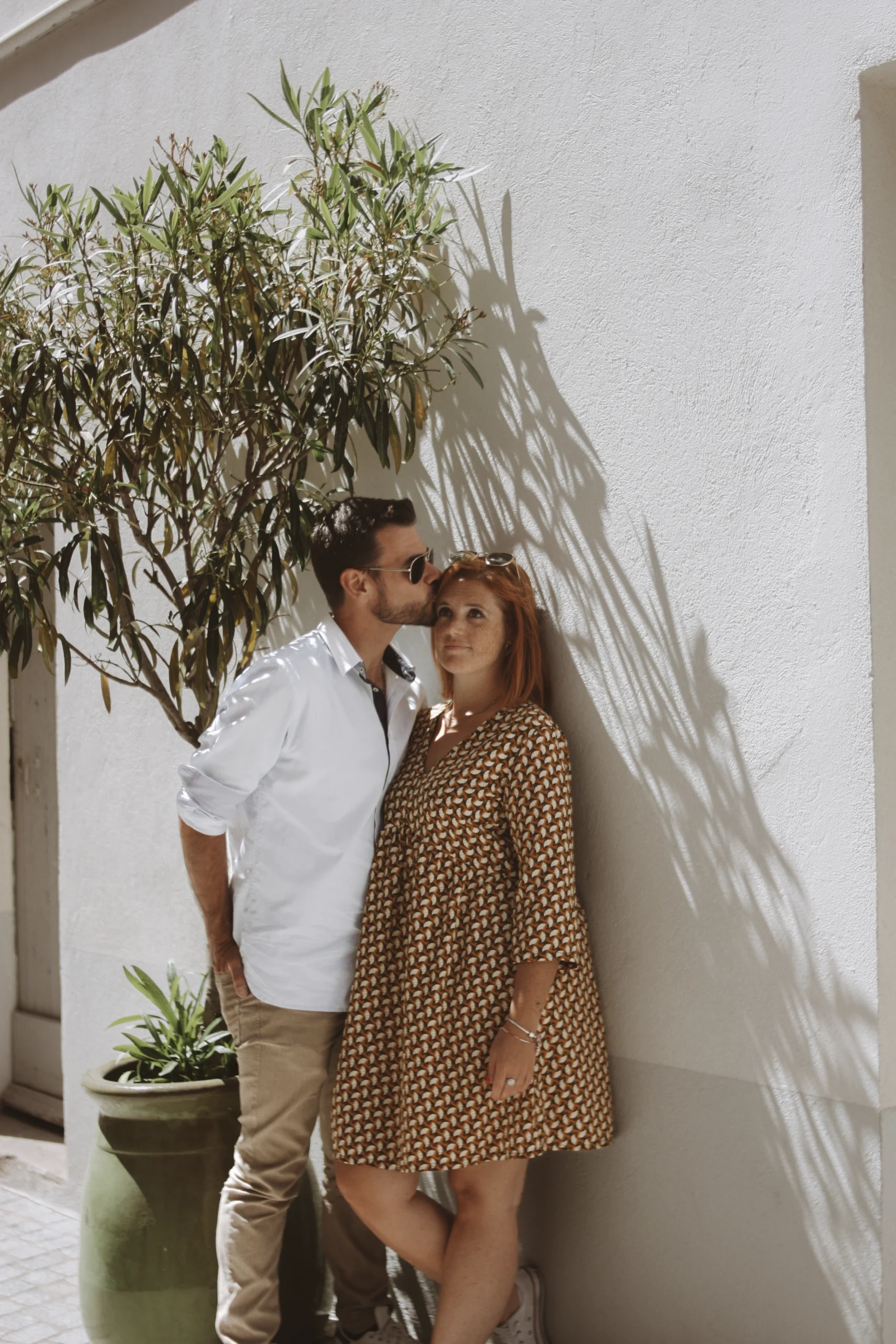 Un couple adossé à un mur blanc en crépis, pendant leur séance engagement dans les rues de Sanary, en Porvence.
