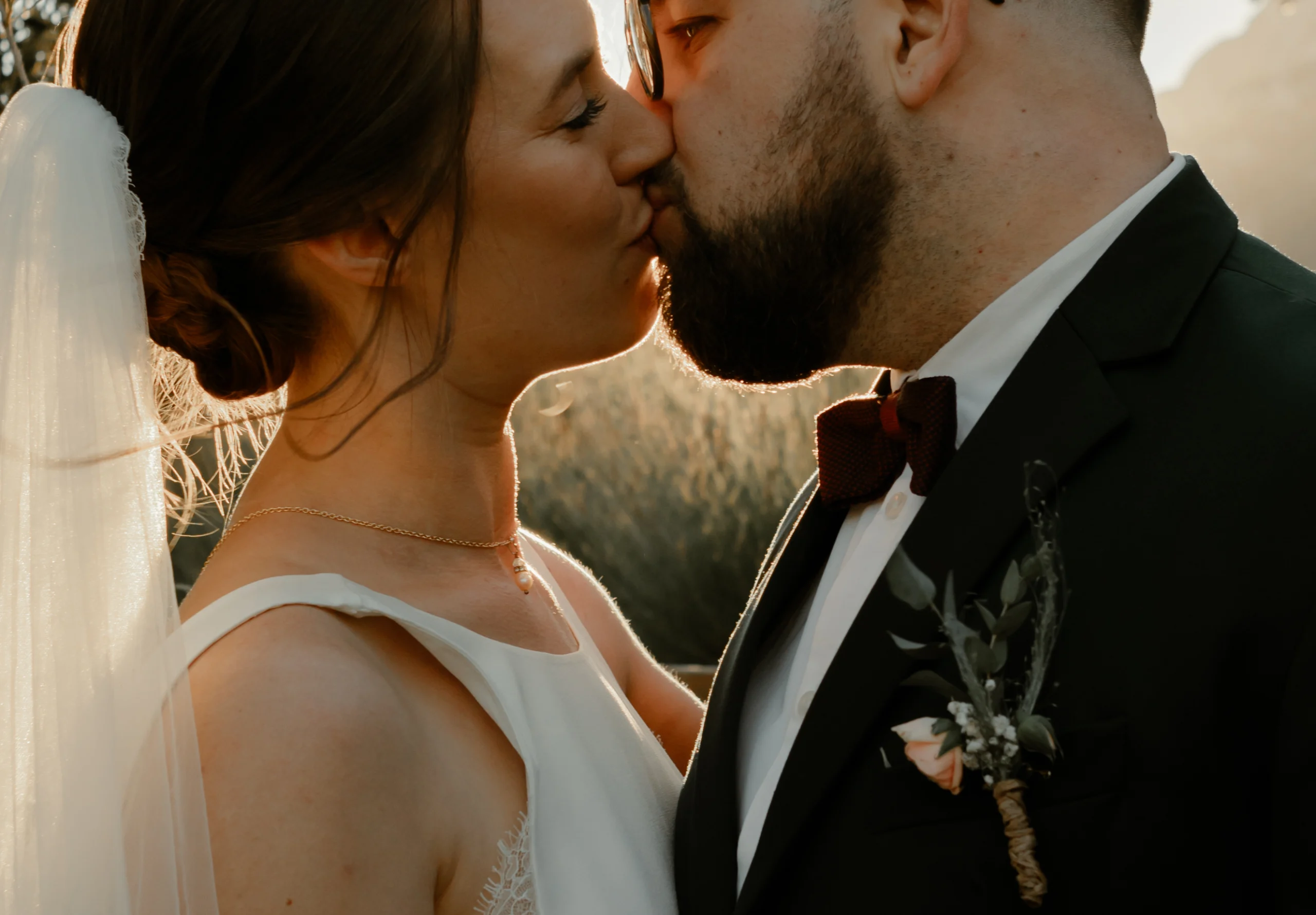 En couple dans leurs tenues de mariages, s'embrassant tendrement au coucher du soleil en Provence, au milieu des oliviers et des lavandes.