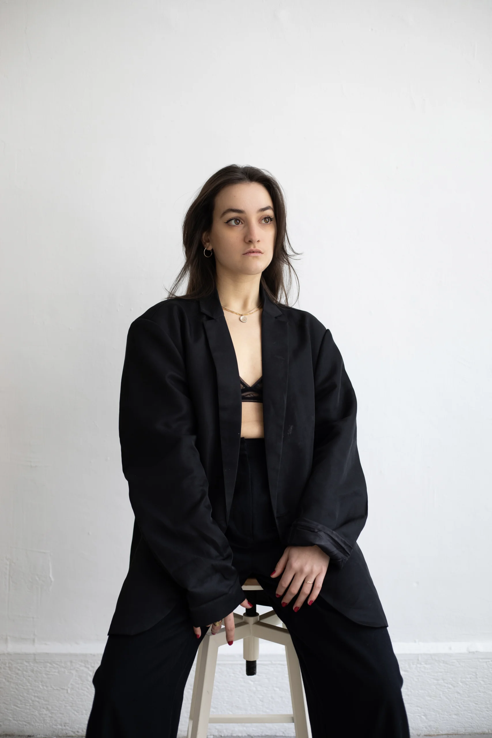 Une jeune femme, dans un tailleur noir, assise sur un tabouret, reprend confiance en elle lors d'une séance photo féminine en intérieur dans le Var.