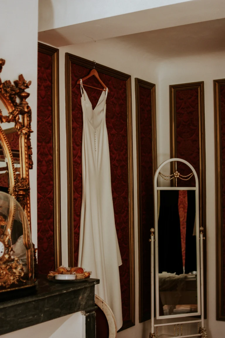 Robe de mariée suspendue sur un mur de velour rouge, lors d'un mariage au Chateau Robernier.