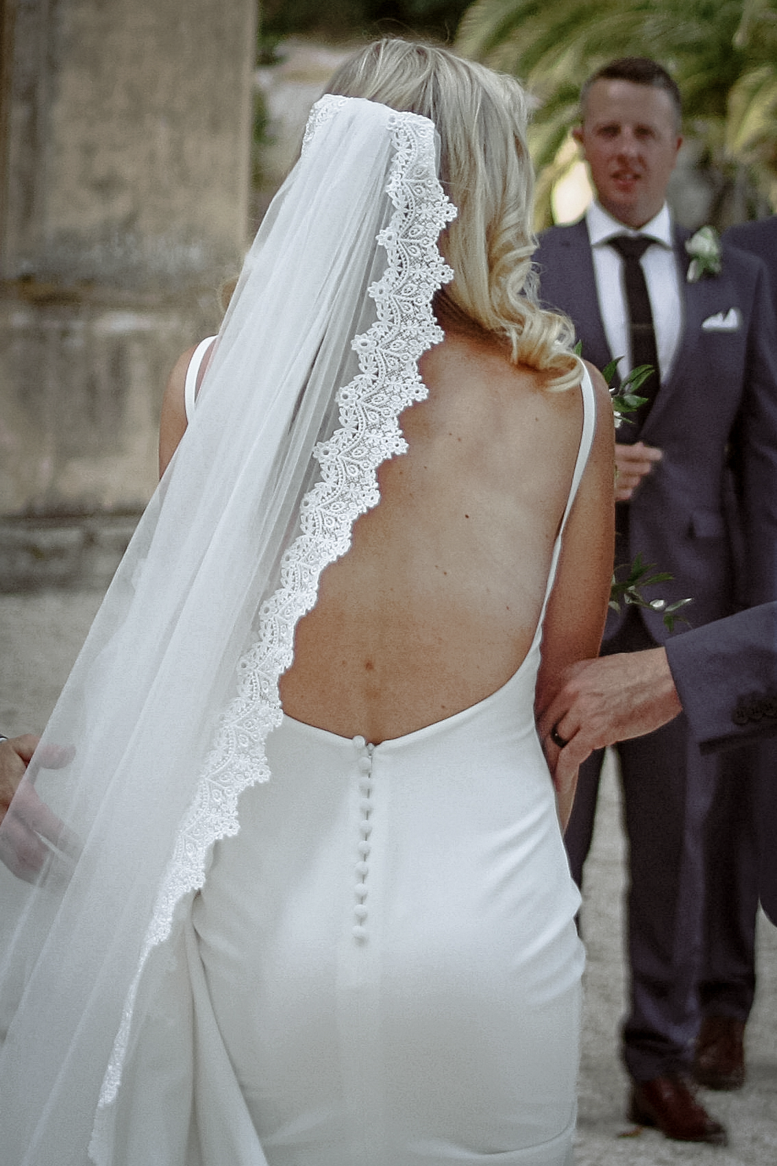Photographie naturelle d'un mariage en Provence, montrant une mariée de dos, vêtue d'une robe dos nu et d'un voile ornée de dentelles.