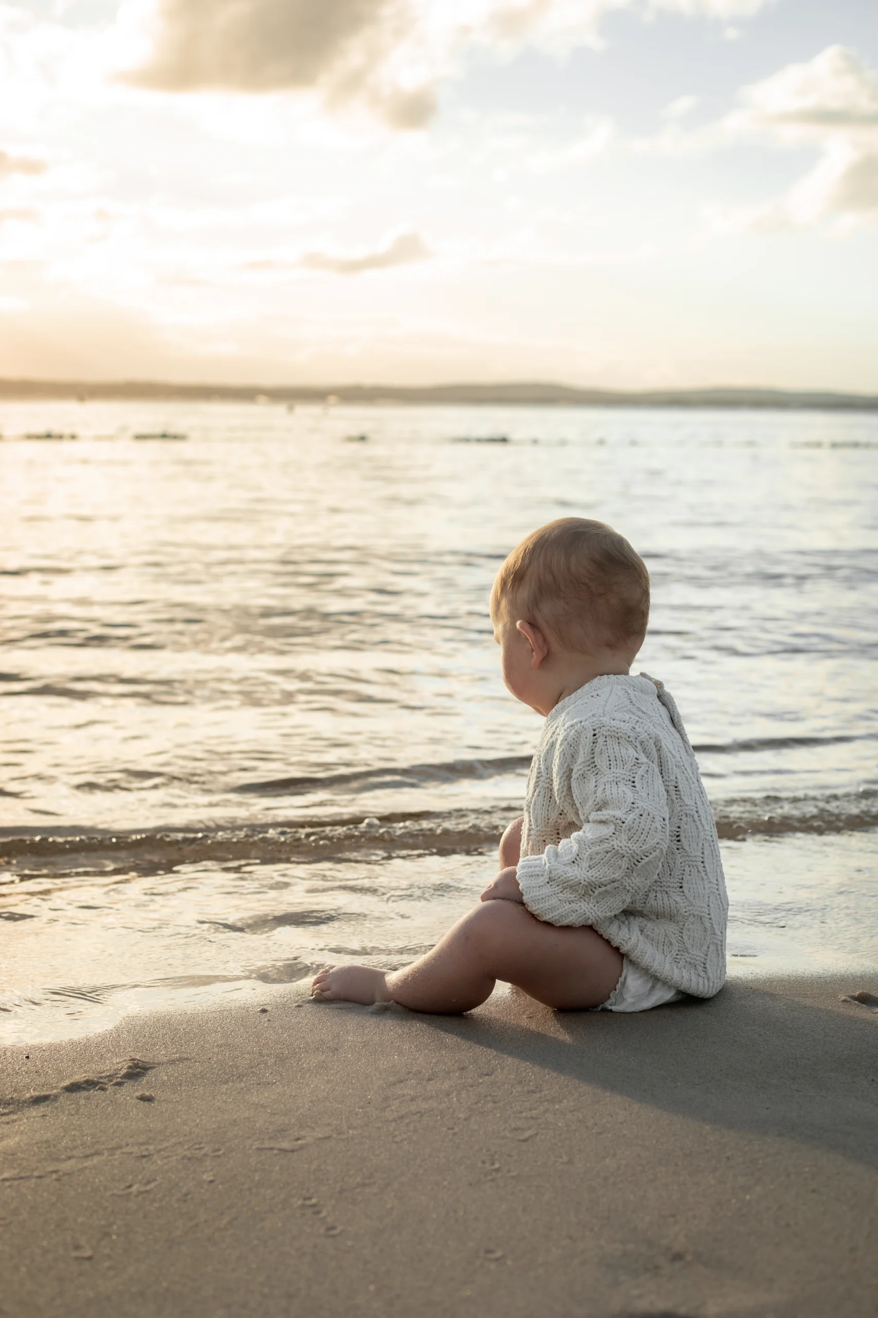 Un bébé d'un an, assis au bord de l'eau, au coucher du soleil. Une séance photo à Hyères douce et documentaire.