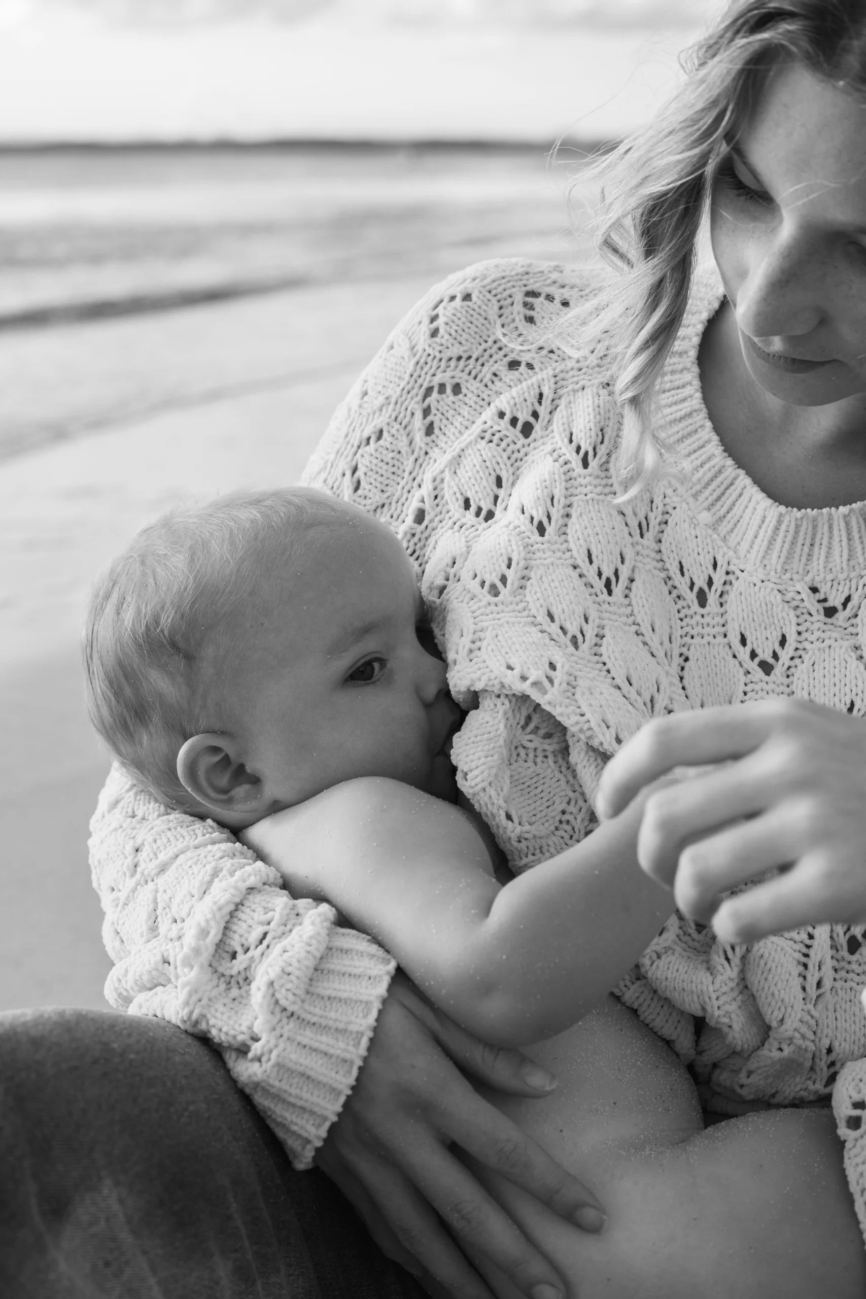 Une mère allaite son bébé en bord de mer. Un moment d'intimité doux et tendre, rempli d'amour. Une photo en noir et blanc, prise par Nolwenn Biannic Photographe
