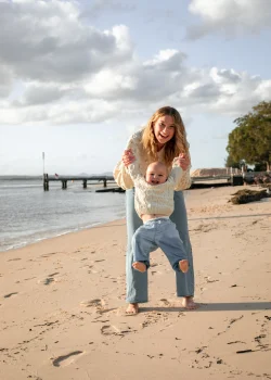 Une mère joue sur la plage avec son fils et le porte dans les airs. Il rit.