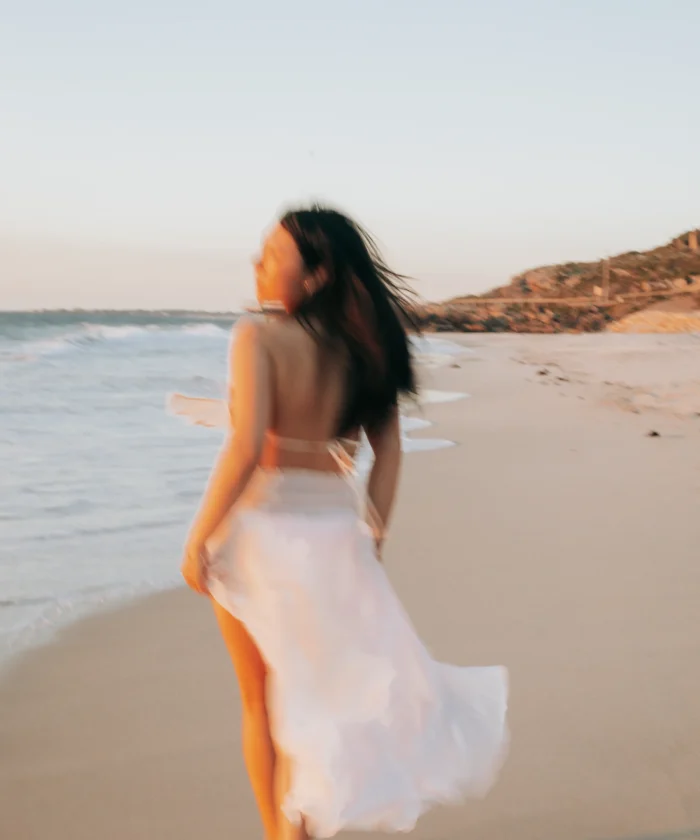Une femme coure sur la plage, les pieds nus. Elle regarde derrière elle avec un air de liberté